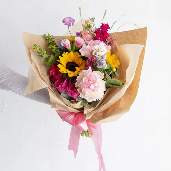 A hand holding a wrapped bouquet of fresh flowers including sunflowers and pink blooms.