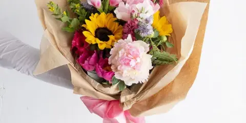 A hand holding a wrapped bouquet of fresh flowers including sunflowers and pink blooms.