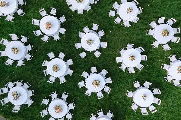 Overhead view of white round tables and chairs set up on a green lawn for an outdoor event.
