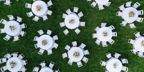 Overhead view of white round tables and chairs set up on a green lawn for an outdoor event.