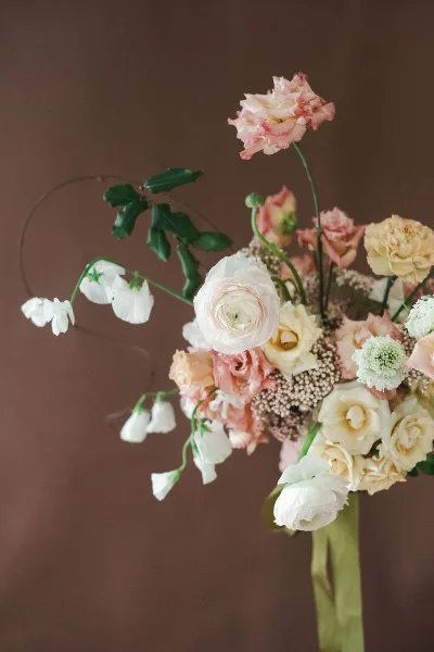 A hand-tied bridal bouquet with garden roses, ranunculus, and trailing lily of the valley against a brown background.