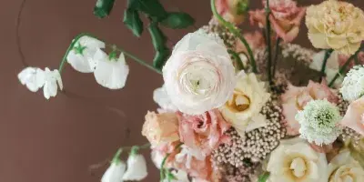 A hand-tied bridal bouquet with garden roses, ranunculus, and trailing lily of the valley against a brown background.