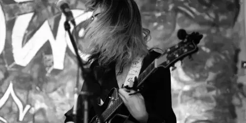 A musician playing an electric guitar at a microphone during a live performance.