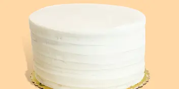 A white, multi-tiered wedding cake with smooth frosting on a gold cake board.