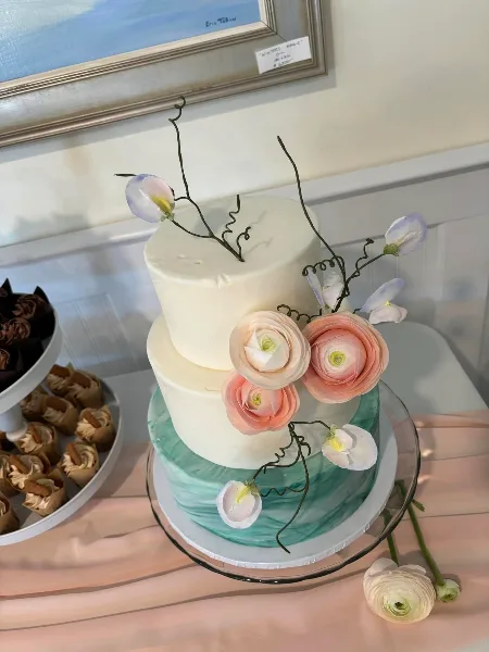 A three-tiered white and green hand-painted wedding cake decorated with sculptural pink and white flowers and delicate vines.