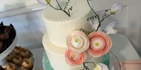 A three-tiered white and green hand-painted wedding cake decorated with sculptural pink and white flowers and delicate vines.