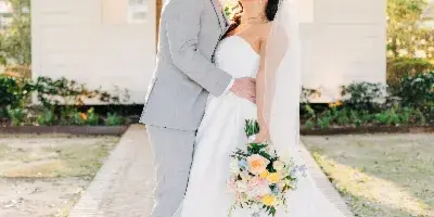 A bride and groom kissing in front of a white chapel building, with the bride holding a colorful bouquet.