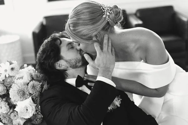 Black and white photograph of a bride and groom kissing, with the bride holding a bouquet of flowers.