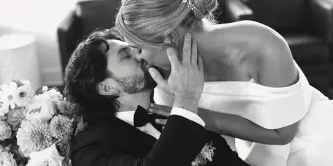 Black and white photograph of a bride and groom kissing, with the bride holding a bouquet of flowers.