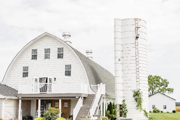 Exterior view of a white round-top roof barn with a silo and outdoor staircase.