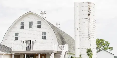 Exterior view of a white round-top roof barn with a silo and outdoor staircase.