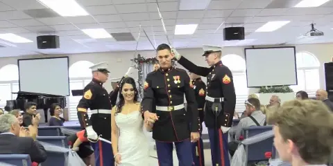 A bride and groom in military dress uniforms walk down the aisle during a wedding ceremony.