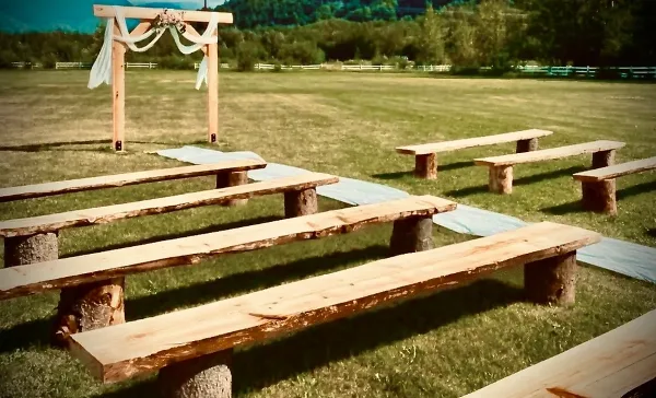 Outdoor wedding ceremony setup with a wooden arch and rustic benches on a grass field