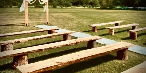 Outdoor wedding ceremony setup with a wooden arch and rustic benches on a grass field