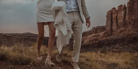 A bride and groom in white wedding attire standing in a red rock desert landscape.