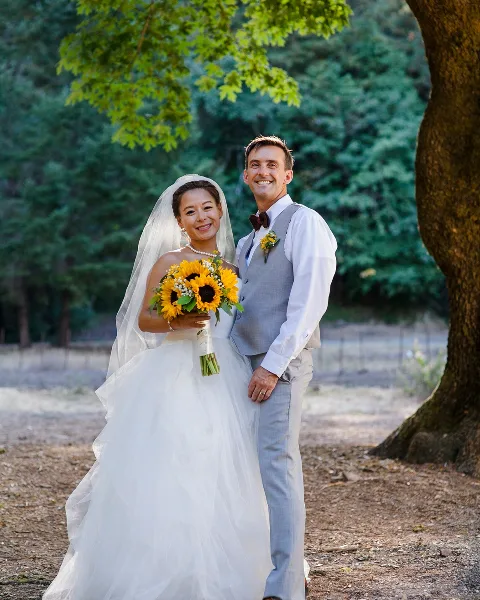 A bride and groom posing outdoors with a sunflower bouquet