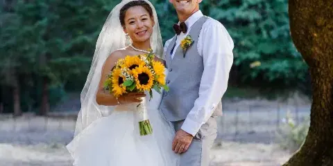 A bride and groom posing outdoors with a sunflower bouquet