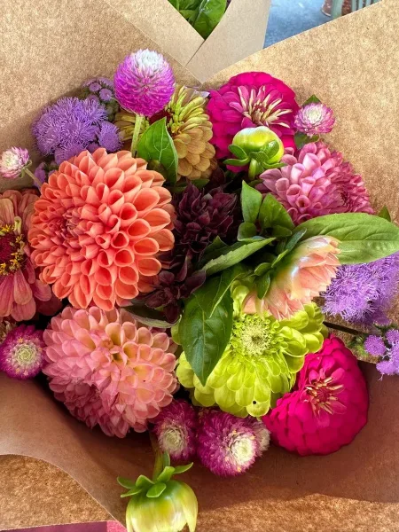 A colorful bouquet of dahlias and other seasonal flowers wrapped in brown kraft paper.