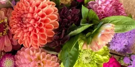 A colorful bouquet of dahlias and other seasonal flowers wrapped in brown kraft paper.