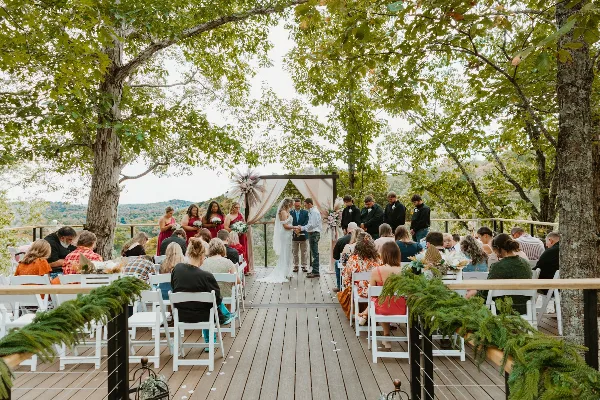 Outdoor wedding ceremony on a wooden deck overlooking a scenic landscape with trees and hills.