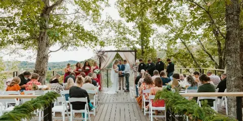 Outdoor wedding ceremony on a wooden deck overlooking a scenic landscape with trees and hills.