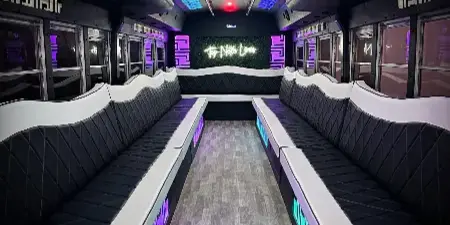 Interior of a party bus with black and white leather seating, LED lighting, and a 'Top Notch Limos' sign on the back wall.