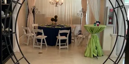 A black metal wedding arch set up in a showroom with a decorated table and chairs in the background.