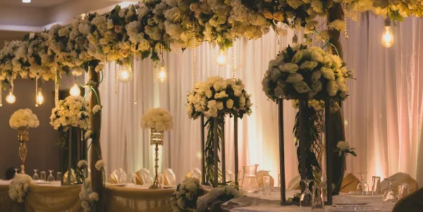 A decorated wedding reception table featuring white floral centerpieces, hanging lights, and draped fabric.