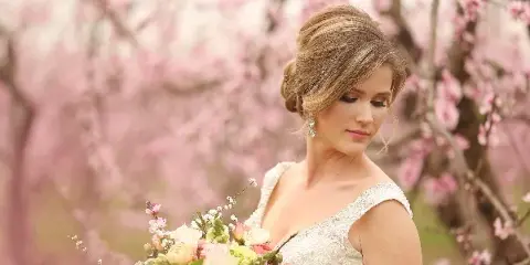 Bride with styled hair and makeup holding a floral bouquet in front of blooming trees
