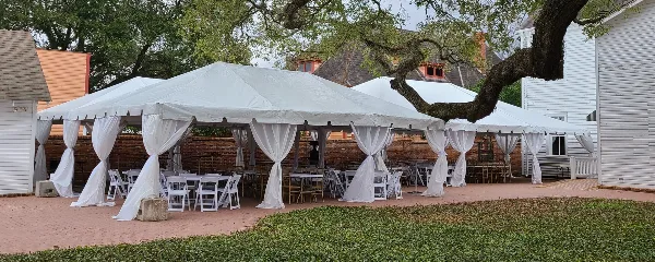 A large white event tent with white draping, tables, and chairs set up outdoors for a wedding or event.