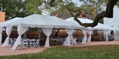 A large white event tent with white draping, tables, and chairs set up outdoors for a wedding or event.