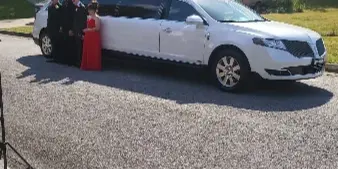 A white stretch limousine parked on a driveway with a group of formally dressed people standing beside it in front of a house.