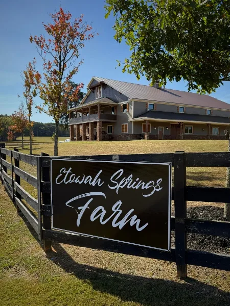 Exterior view of a two-story farm venue building with a wooden fence and a sign reading Etowah Springs Farm