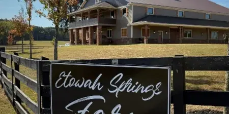 Exterior view of a two-story farm venue building with a wooden fence and a sign reading Etowah Springs Farm