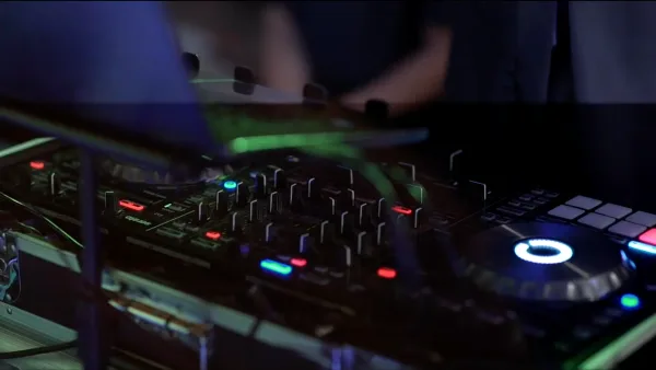 Close-up of a DJ mixing board and turntable with illuminated controls in a dark room.