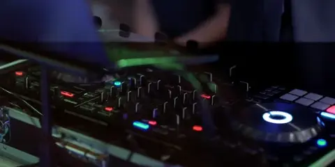Close-up of a DJ mixing board and turntable with illuminated controls in a dark room.