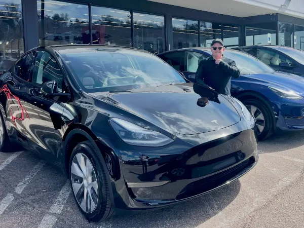 A man standing next to a black Tesla Model Y in a parking lot.