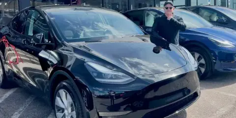 A man standing next to a black Tesla Model Y in a parking lot.