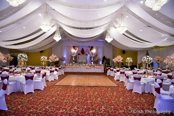Interior view of a large wedding event hall with a central dance floor, round tables, and ceiling drapery.