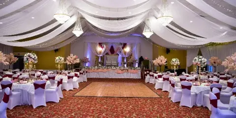 Interior view of a large wedding event hall with a central dance floor, round tables, and ceiling drapery.