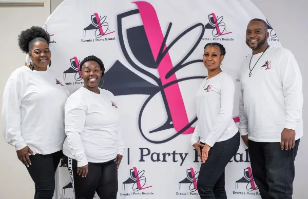 Four team members of LB's Rental standing in front of a branded backdrop featuring the company logo and the text 'Events | Party Rental'.