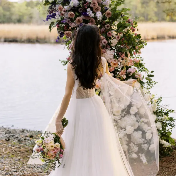 Bride holding a bouquet standing near a large floral installation by the water