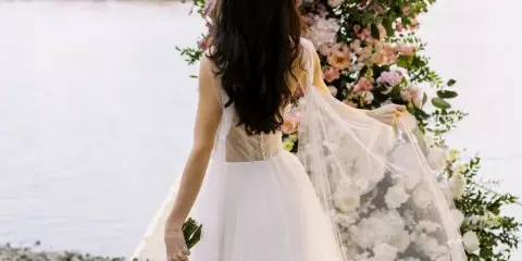 Bride holding a bouquet standing near a large floral installation by the water