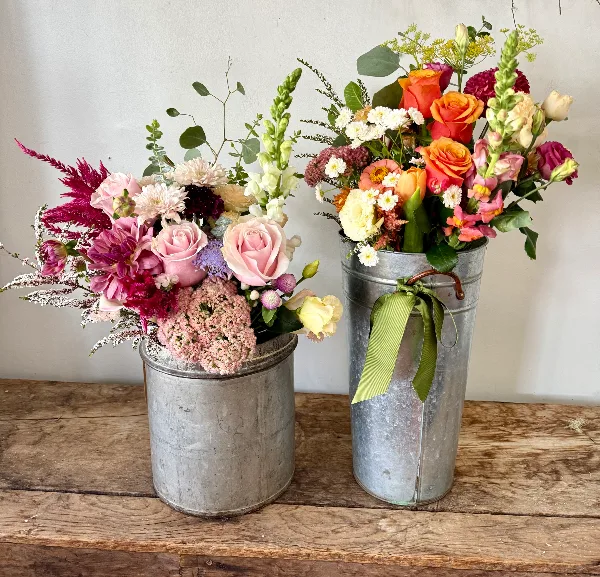 Two fresh floral arrangements in galvanized metal buckets on a wooden table