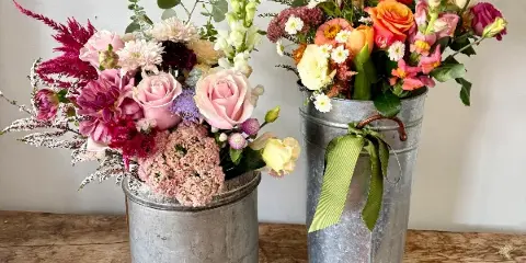 Two fresh floral arrangements in galvanized metal buckets on a wooden table