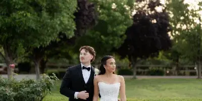 A bride and groom standing together in a garden setting, with the groom in a black tuxedo and the bride in a white wedding dress holding a bouquet.