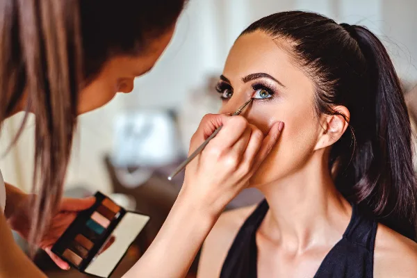 A makeup artist applying eye makeup to a woman using a brush and eyeshadow palette.