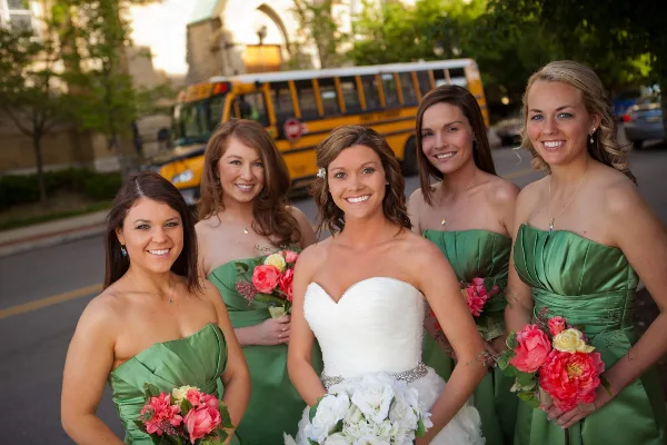 A bride and four bridesmaids in green dresses standing in front of a yellow school bus.