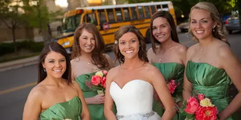 A bride and four bridesmaids in green dresses standing in front of a yellow school bus.
