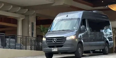 A gray Mercedes-Benz Sprinter shuttle van with SpeediShuttle branding parked at a hotel entrance.